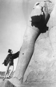 Scavi archeologici. Una giovane ballerina in posa davanti a una statua trovata durante gli scavi archeologici nelle rovine di Karnak. Egitto. Luxor, 1930 - AA15012