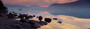 David Noton Dawn, Dawn is breaking on the far misty shore of Derwentwater, with rocks standing out starkly on the near shore, Cumbria.
