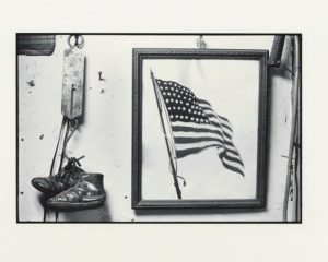 Black and white photo by Laura Volkerding, History's office, 1964 shows a drawing of american usa flad with a picture frame around it and hanging shoes