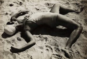 Photo of swimmer laying on beach sand in odd pose