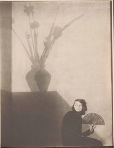 early 20th century photo by Edward Weston sepia tones woman seated with fan shadow of vase with flowers