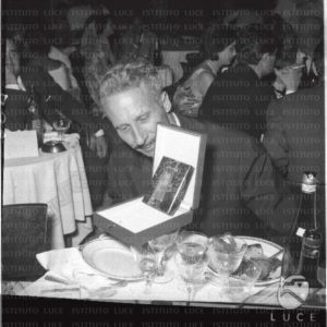Il regista Jacques Becker seduto ad un tavolo che osserva il premio ricevuto per il miglior film. Piano medio. Consegna dei nastri d'argento. Roma. 14.07.1956
