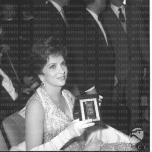Gina Lollobrigida seduta in platea mostra il Nastro d'Argento appena ricevuto - piano medio. Prima del film 'Il Gattopardo' e premiazione dei Nastri d'argento. Cinema Barberini di Roma. 27.03.1963