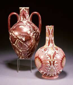 A pink, ruby and gold lustre vase and a ruby lustre vase with ferocious reptiles amongst stylised foliage. Both designed by William De Morgan (1839-1917). 27cm high. - PC28300